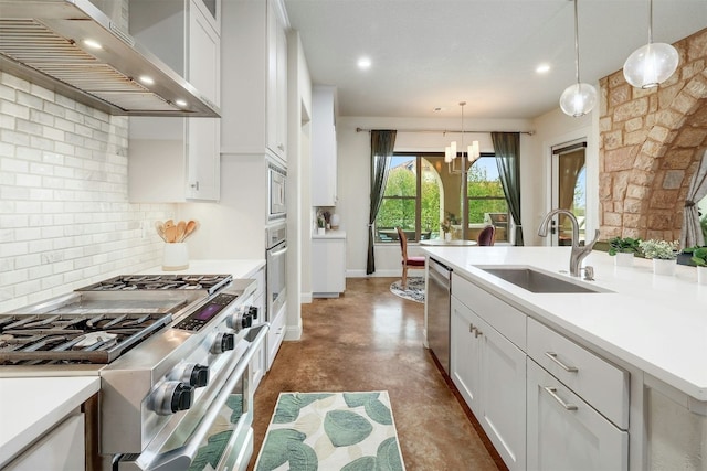 kitchen featuring a sink, light countertops, wall chimney range hood, hanging light fixtures, and appliances with stainless steel finishes