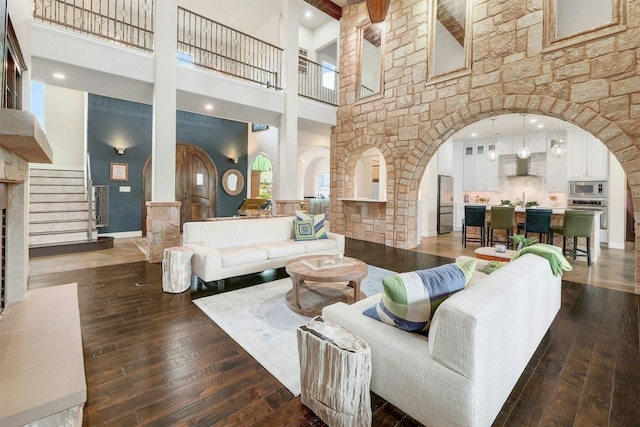 living area featuring dark wood-type flooring, baseboards, arched walkways, and a towering ceiling