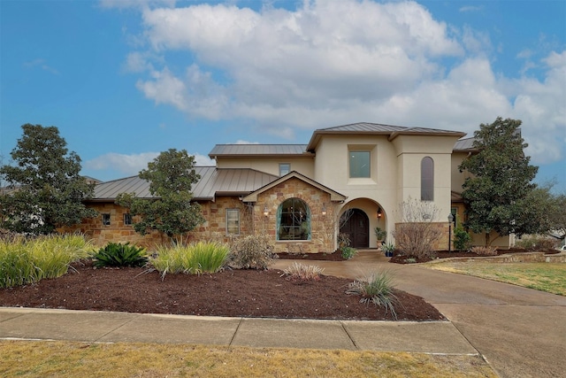 view of front facade featuring metal roof, stone siding, driveway, stucco siding, and a standing seam roof