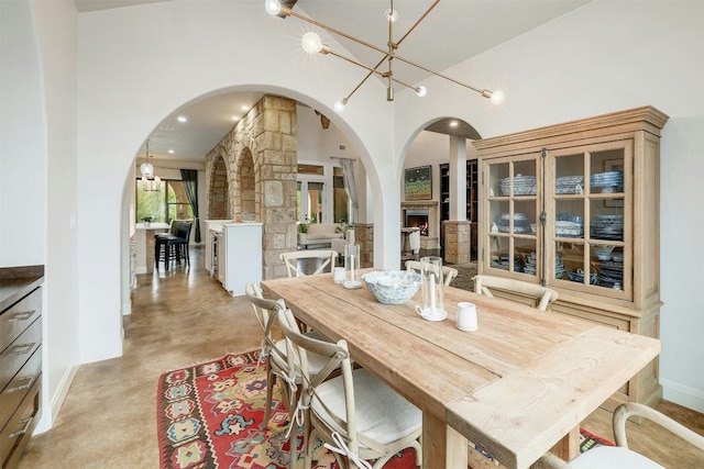 dining room with arched walkways, a fireplace, a high ceiling, a chandelier, and concrete flooring