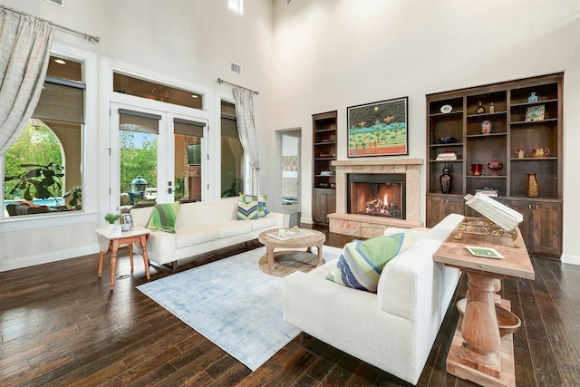 living room with a warm lit fireplace, dark wood-style flooring, visible vents, and french doors