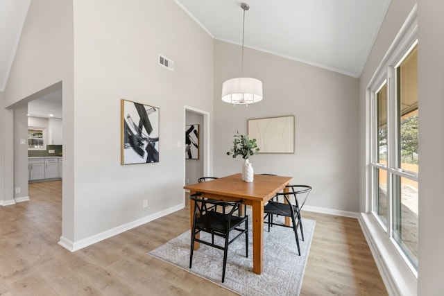 dining space with visible vents, light wood-style flooring, ornamental molding, high vaulted ceiling, and baseboards