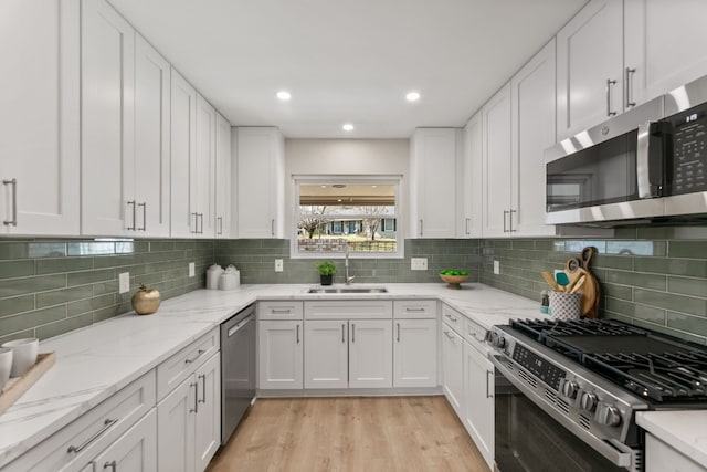 kitchen featuring light stone counters, stainless steel appliances, light wood-style floors, white cabinetry, and a sink