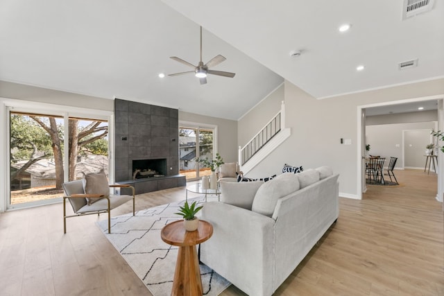 living area featuring a fireplace, light wood finished floors, visible vents, vaulted ceiling, and stairs