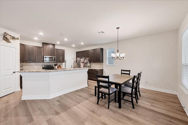 kitchen with a center island with sink, dark brown cabinets, hanging light fixtures, light hardwood / wood-style flooring, and appliances with stainless steel finishes