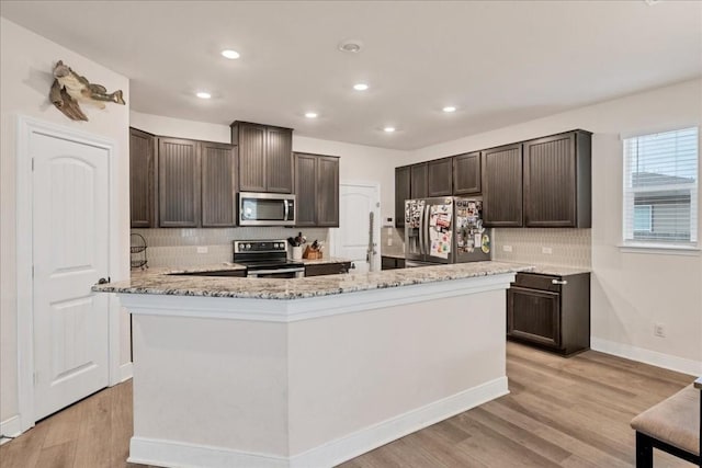 kitchen featuring an island with sink, appliances with stainless steel finishes, dark brown cabinets, and light wood-type flooring