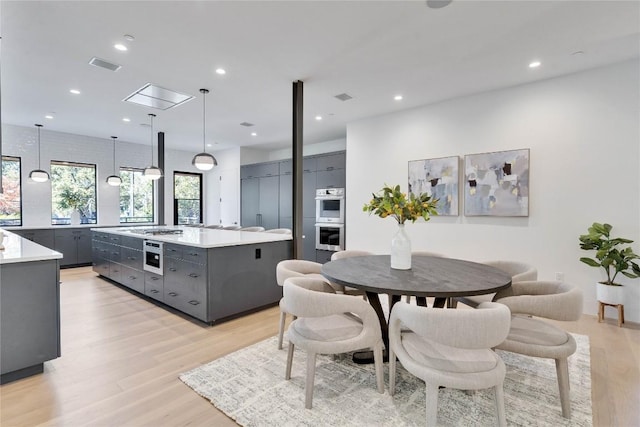 kitchen featuring hanging light fixtures, light wood-type flooring, gray cabinets, double oven, and a kitchen island