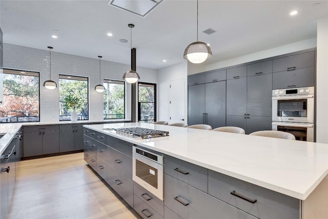 kitchen featuring appliances with stainless steel finishes, a large island, gray cabinetry, and decorative light fixtures