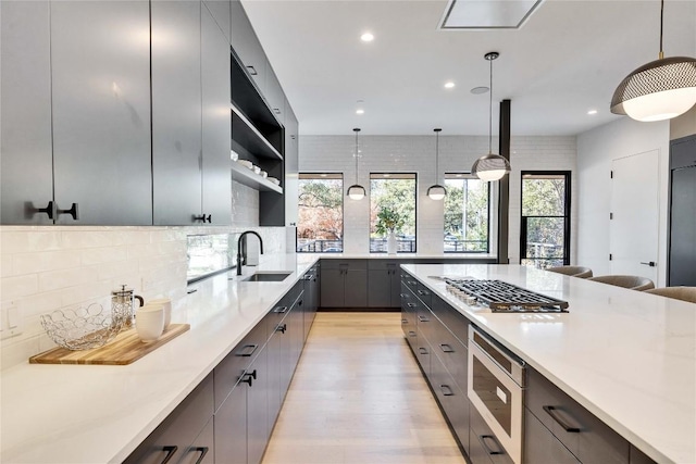 kitchen with appliances with stainless steel finishes, sink, backsplash, hanging light fixtures, and light hardwood / wood-style floors