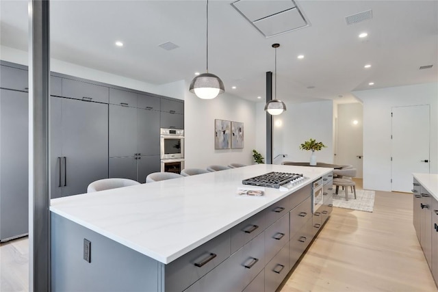 kitchen with gray cabinets, appliances with stainless steel finishes, hanging light fixtures, light hardwood / wood-style floors, and a spacious island