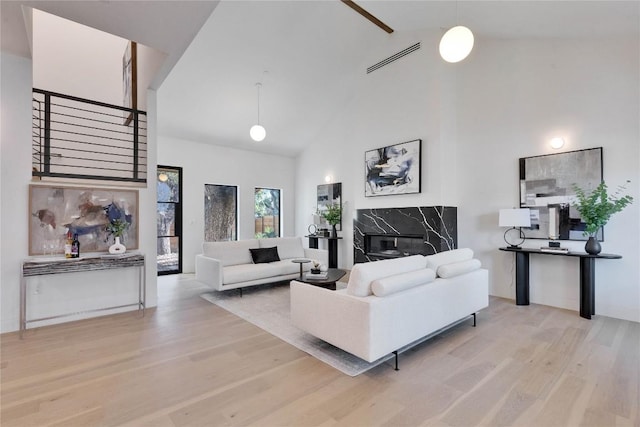 living room featuring a high end fireplace, high vaulted ceiling, and light wood-type flooring