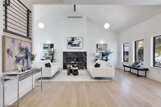 living room with high vaulted ceiling, light hardwood / wood-style floors, and a premium fireplace