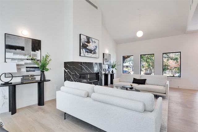 living room with high vaulted ceiling, a fireplace, and light hardwood / wood-style floors