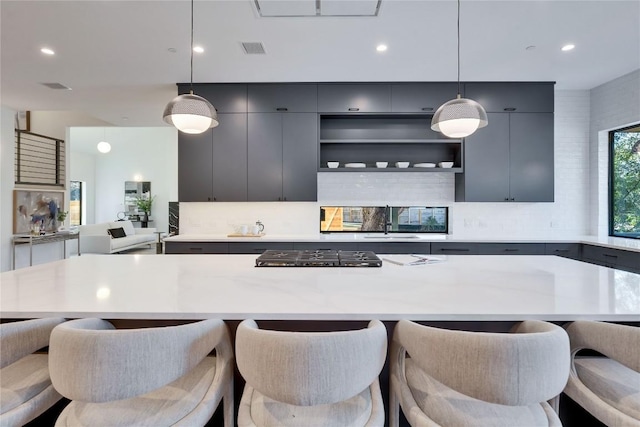 kitchen featuring hanging light fixtures, decorative backsplash, stainless steel gas cooktop, and a kitchen bar