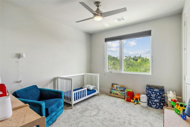 carpeted bedroom featuring a crib and ceiling fan