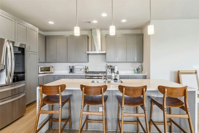 kitchen featuring appliances with stainless steel finishes, pendant lighting, gray cabinetry, and wall chimney exhaust hood