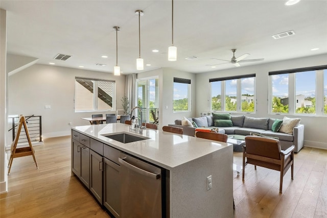 kitchen with sink, light hardwood / wood-style flooring, a center island with sink, decorative light fixtures, and stainless steel dishwasher