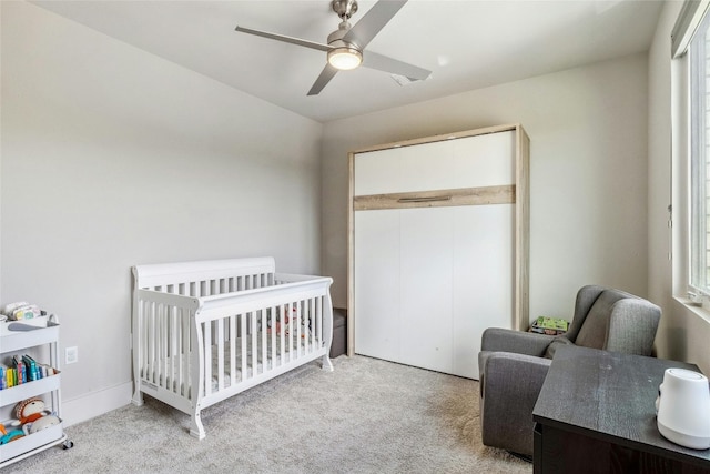 carpeted bedroom with a crib, ceiling fan, multiple windows, and a closet