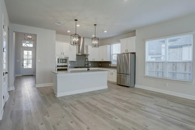 kitchen with pendant lighting, white cabinetry, a kitchen island with sink, stainless steel appliances, and wall chimney range hood