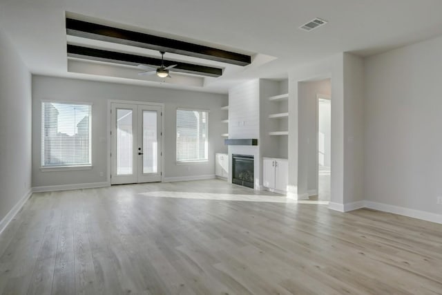 unfurnished living room featuring plenty of natural light, built in features, a fireplace, and french doors