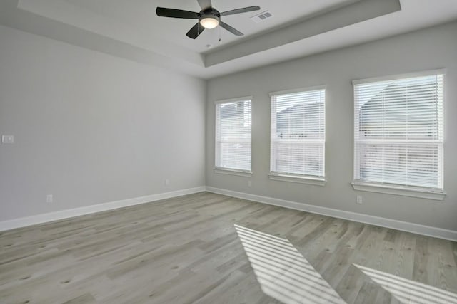 spare room featuring a raised ceiling, ceiling fan, and light wood-type flooring