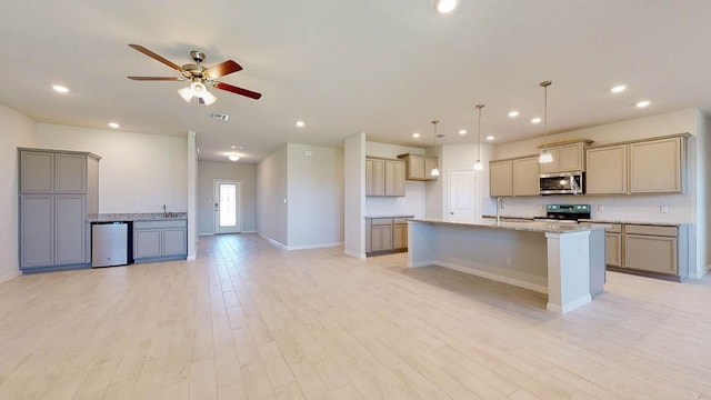 kitchen featuring light stone countertops, light hardwood / wood-style flooring, a center island with sink, and electric stove