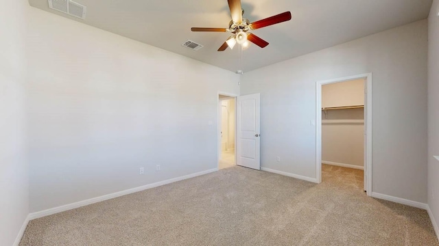 unfurnished bedroom featuring a spacious closet, light colored carpet, a closet, and ceiling fan