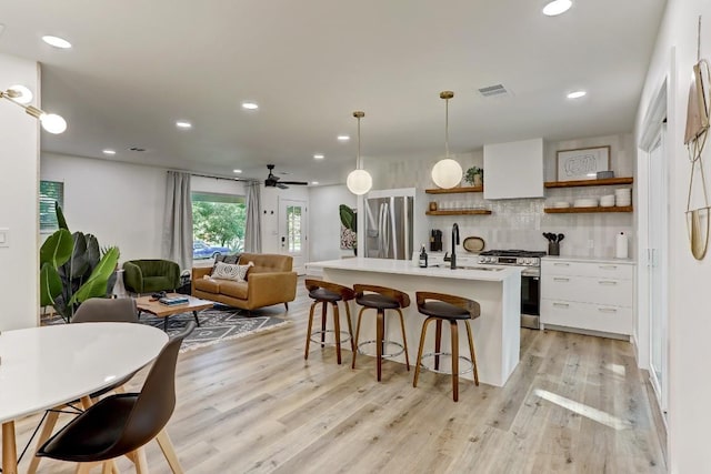 kitchen with appliances with stainless steel finishes, a kitchen island with sink, decorative backsplash, white cabinets, and decorative light fixtures