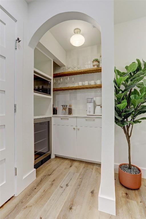 bar with white cabinetry, light hardwood / wood-style floors, black microwave, and beverage cooler