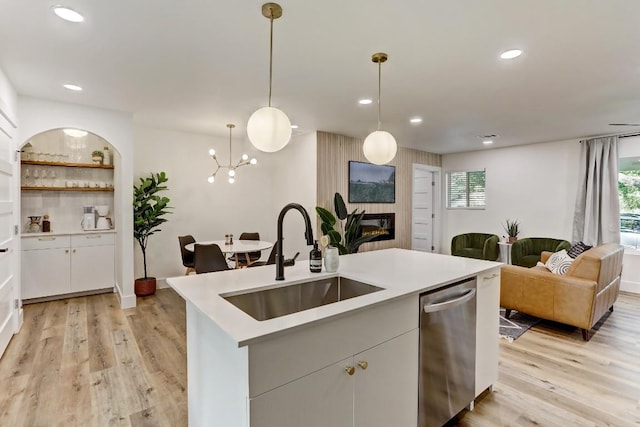 kitchen with decorative light fixtures, dishwasher, sink, white cabinets, and a kitchen island with sink