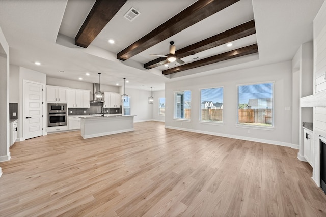 unfurnished living room with beamed ceiling, ceiling fan, a raised ceiling, and light hardwood / wood-style flooring