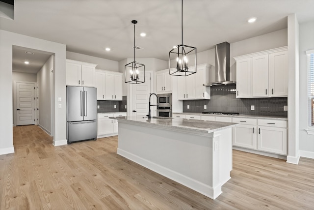 kitchen with appliances with stainless steel finishes, a kitchen island with sink, white cabinets, and wall chimney exhaust hood