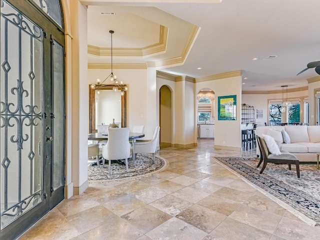 entryway with crown molding, plenty of natural light, a tray ceiling, and a chandelier