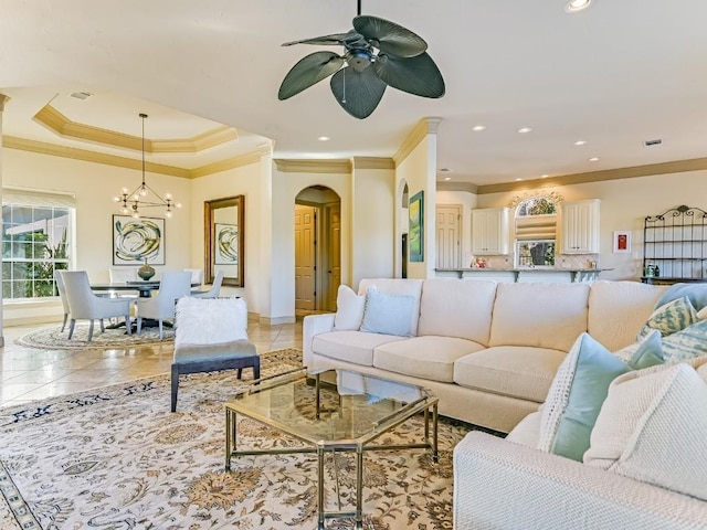 tiled living room featuring crown molding, ceiling fan with notable chandelier, and a raised ceiling