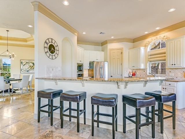 kitchen featuring a breakfast bar area, backsplash, stainless steel appliances, light stone countertops, and white cabinets