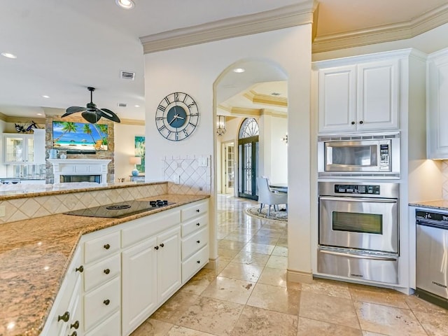 kitchen featuring appliances with stainless steel finishes, tasteful backsplash, white cabinetry, ornamental molding, and light stone countertops