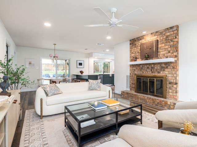 living area featuring baseboards, visible vents, wood finished floors, a brick fireplace, and recessed lighting