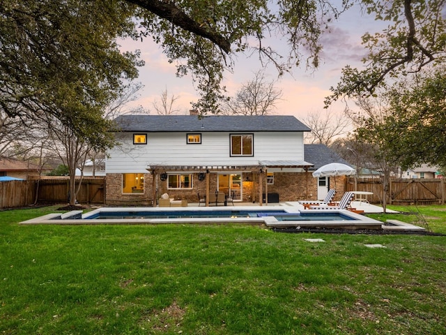 back house at dusk featuring a fenced in pool, a patio, and a yard