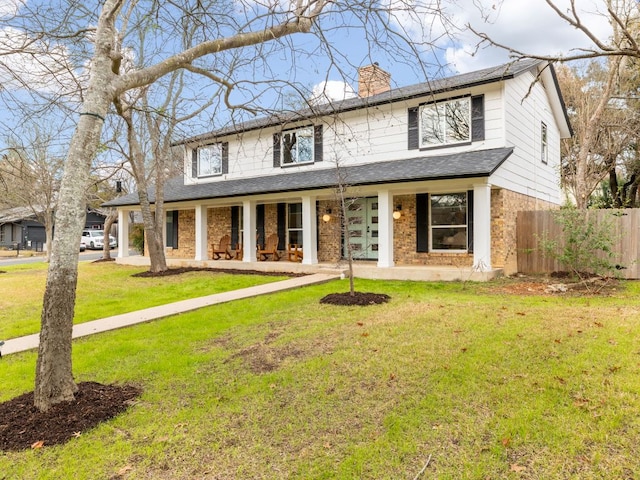 view of front of home with brick siding, a chimney, covered porch, a front yard, and fence