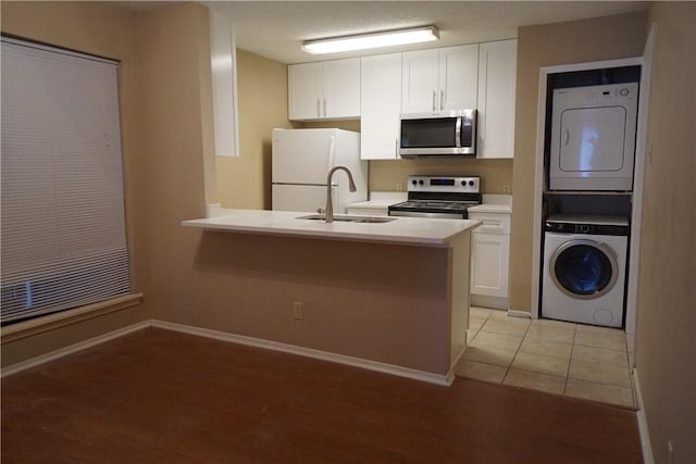 kitchen with sink, white cabinetry, stainless steel appliances, stacked washer / dryer, and kitchen peninsula