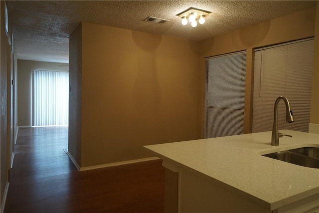 kitchen featuring dark hardwood / wood-style floors, sink, a center island with sink, and a textured ceiling