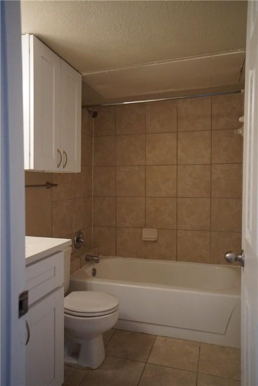 full bathroom with tile patterned floors, toilet, a textured ceiling, vanity, and tiled shower / bath combo