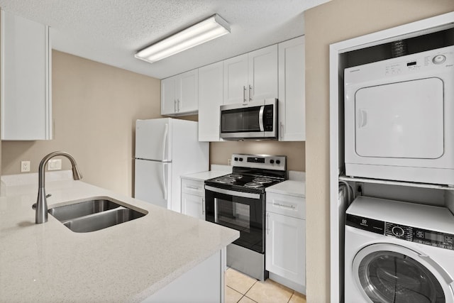 kitchen with appliances with stainless steel finishes, sink, white cabinetry, and stacked washer and clothes dryer