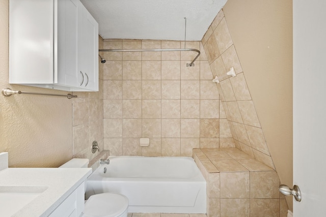 full bathroom featuring a textured ceiling, toilet, vanity, and tiled shower / bath combo