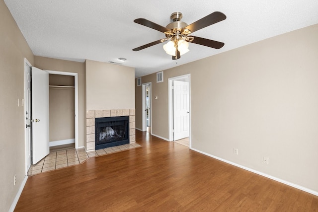 unfurnished living room with ceiling fan, light hardwood / wood-style flooring, a tile fireplace, and a textured ceiling