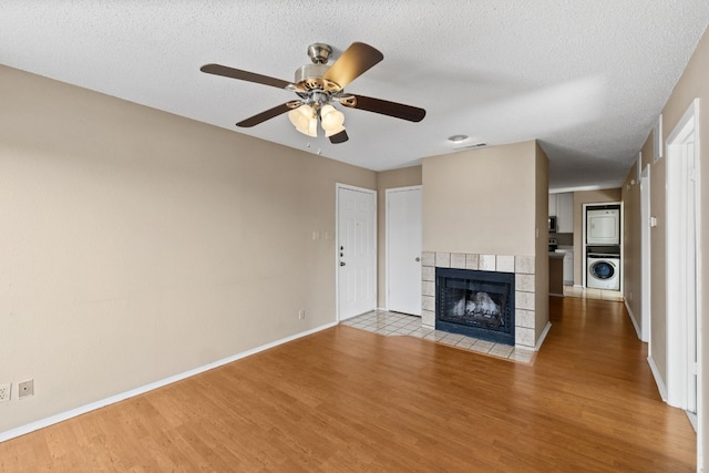 unfurnished living room with a tile fireplace, light wood-type flooring, washer / dryer, and a textured ceiling