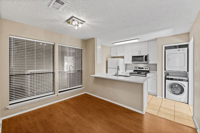 kitchen with stacked washing maching and dryer, appliances with stainless steel finishes, white cabinets, and kitchen peninsula