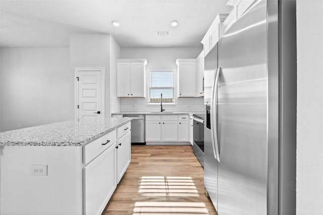 kitchen with stainless steel appliances, light stone countertops, a kitchen island, and white cabinets