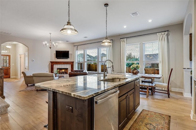 kitchen with sink, dark brown cabinets, stainless steel dishwasher, an island with sink, and a tile fireplace