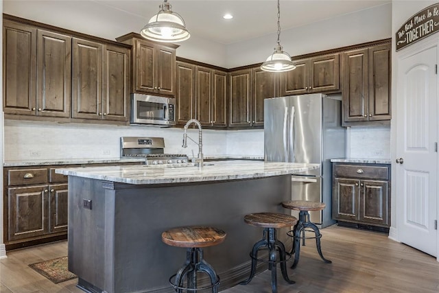 kitchen with hanging light fixtures, appliances with stainless steel finishes, dark brown cabinets, and a center island with sink